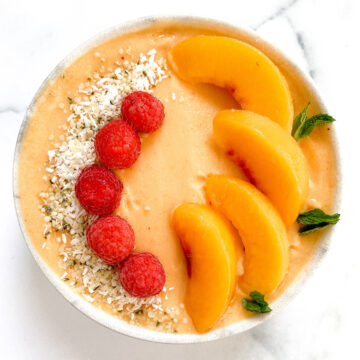 A vegan fuzzy peach smoothie bowl topped with peach slices, mint, and raspberries.
