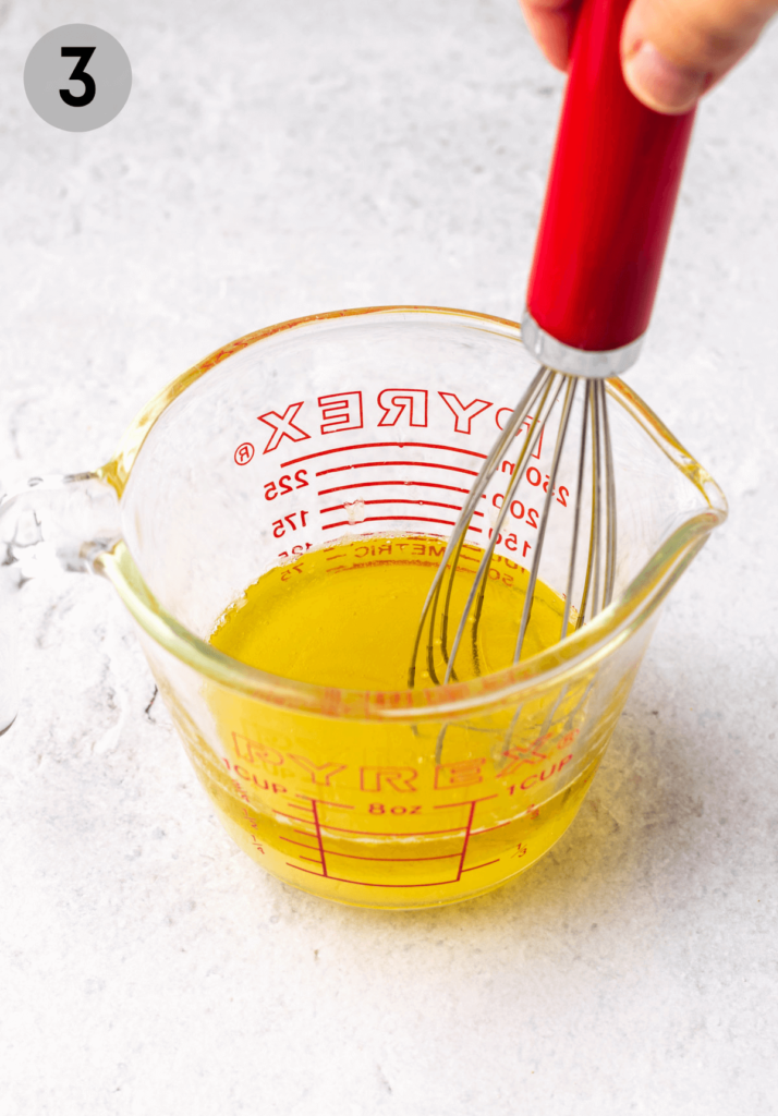 a whisk stirring dressing in a measuring cup