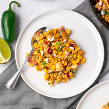 mexican street corn salad on a white plate with jalapeno and lime on the side