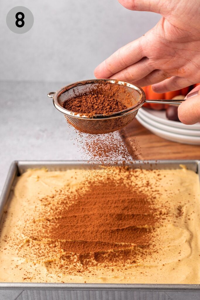 hand sifting cocoa powder over pumpkin tiramisu