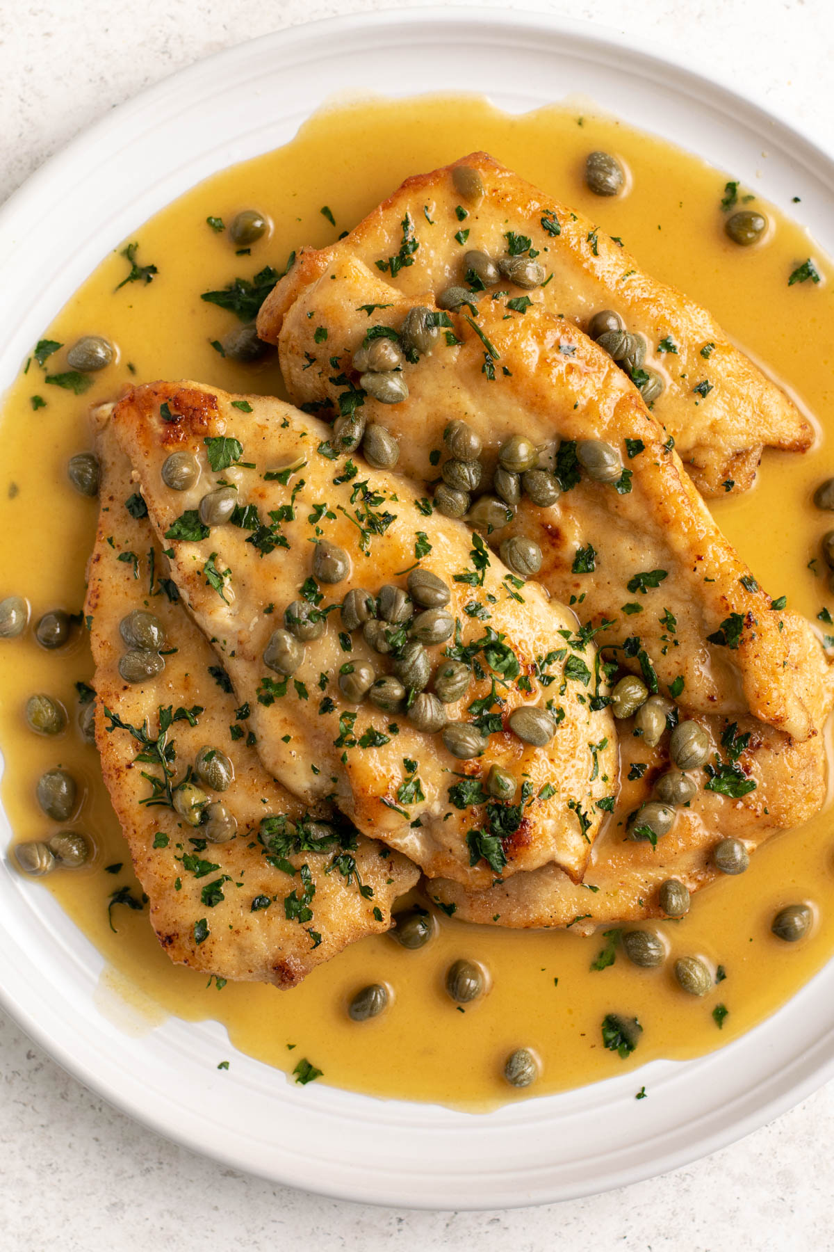 top view of chicken piccata with sauce on a white plate.