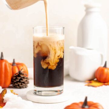 pouring pumpkin cold foam into a glass of cold brew.