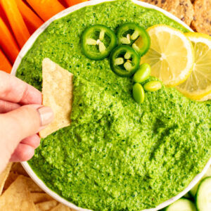 hand dipping a tortilla chip in kale edamame dip.