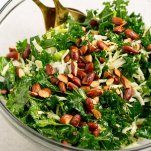 kale salad topped with almonds in a glass bowl.