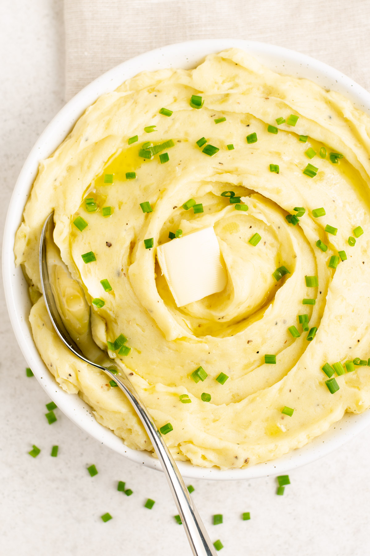 top view of a bowl of mashed potatoes topped with chives and a pad of butter.