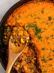 wooden spoon scooping sweet potato shepherd's pie from a cast iron skillet.