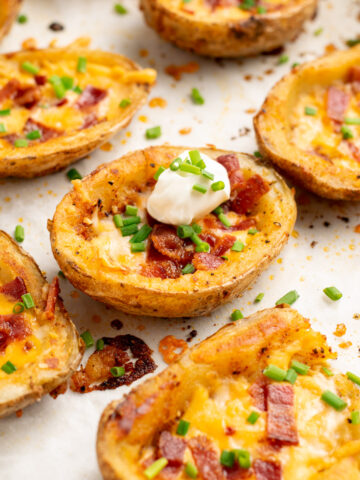 loaded potato skins on a baking sheet topped with chives and sour cream.