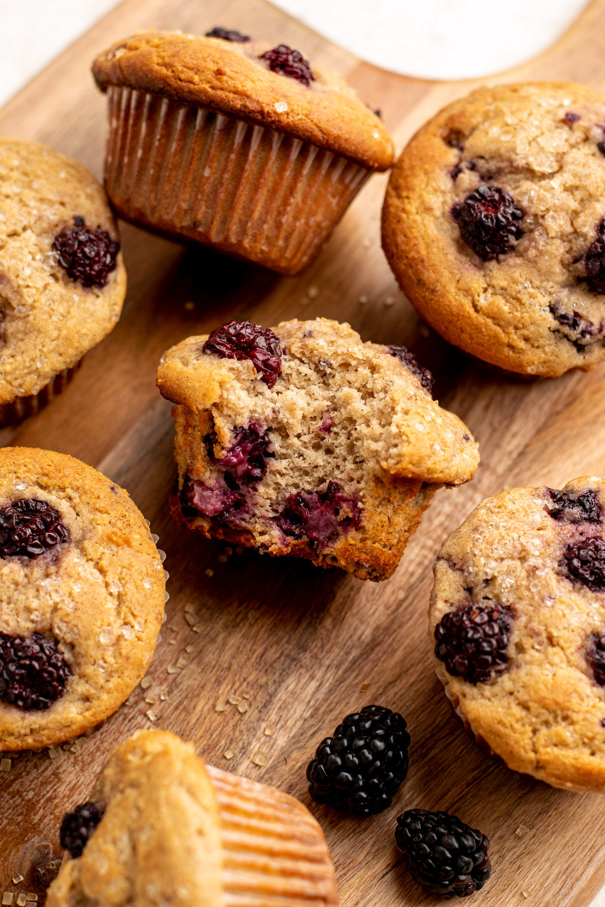 blackberry muffins on a wood board, the middle with a bite missing.