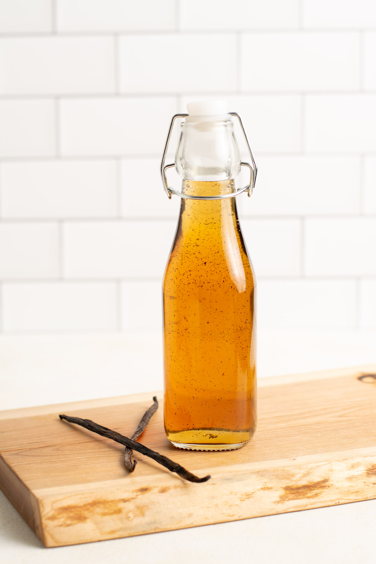 a jar of vanilla simple syrup and 2 vanilla beans on a wood board.