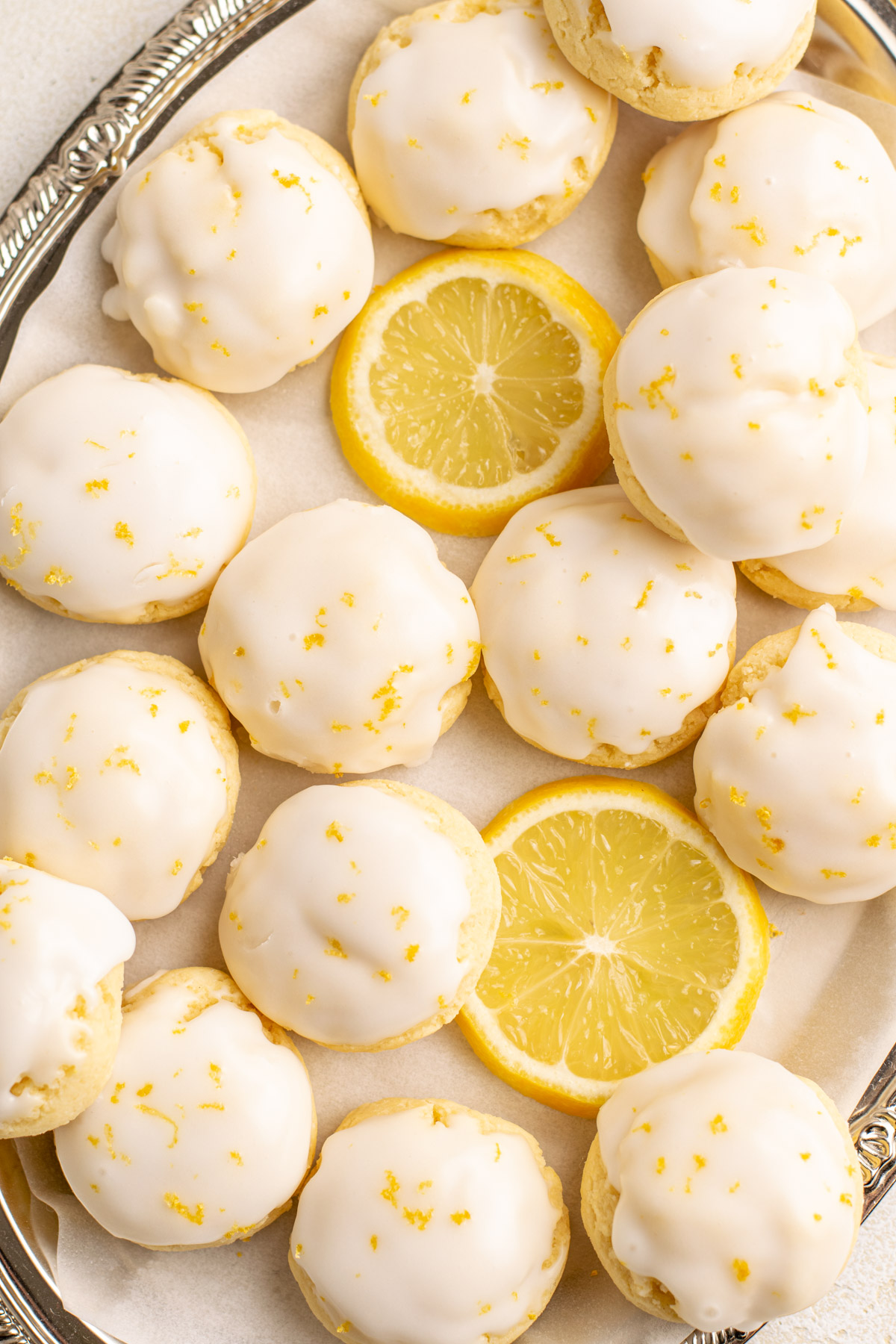 top view of gluten free lemon cookies with 2 lemon slices on a silver tray.