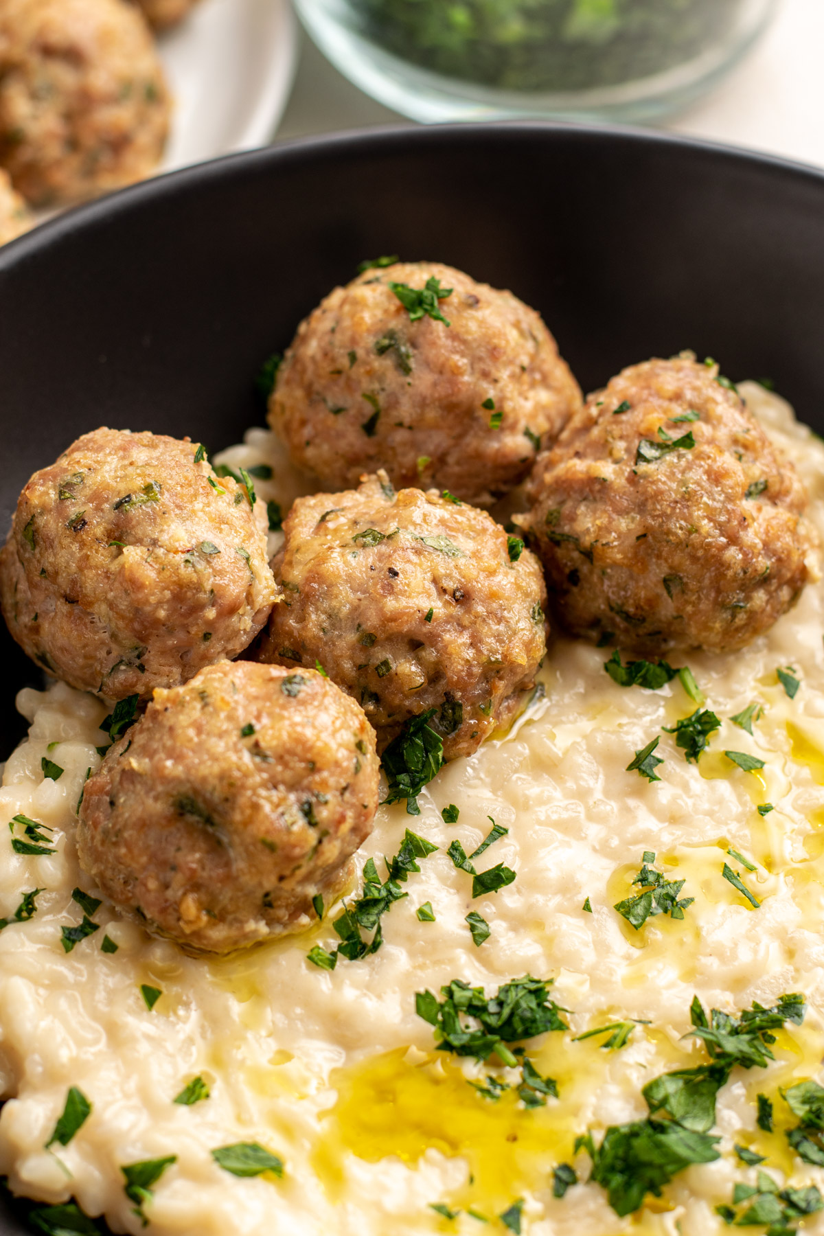 close up of gluten free turkey meatballs on a bed of risotto in a black bowl.