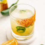 skinny spicy margarita in a tajin rimmed glass with a jalapeno in the background.