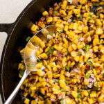 metal spoon in a cast iron skillet filled with charred corn.