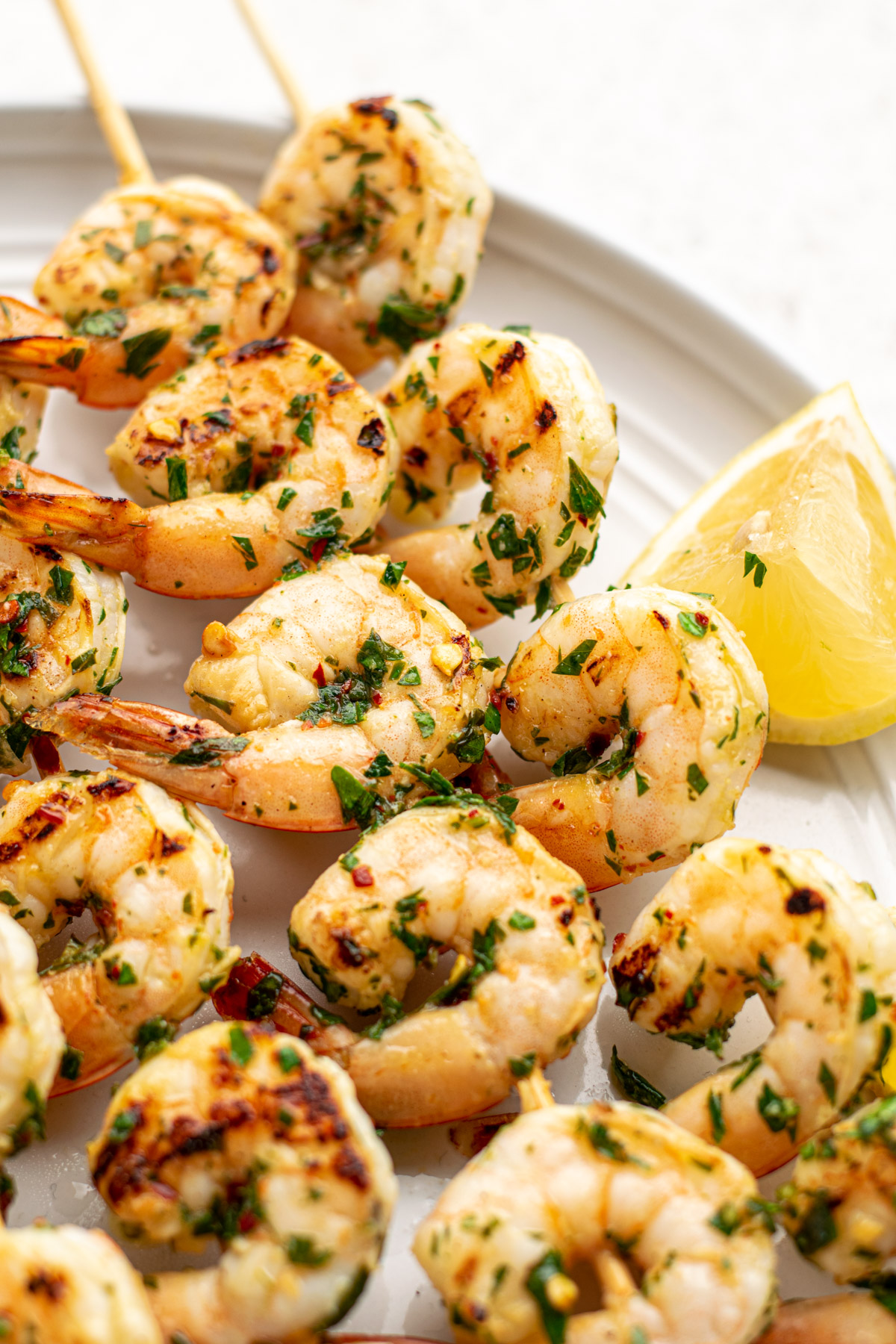 chimichurri shrimp skewers on a white plate with a lemon wedge.
