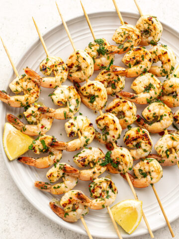 chimichurri shrimp skewers on a white plate with lemon slices.