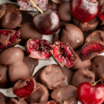 close up of chocolate covered cherries, some cut in half to reveal the cherry inside.