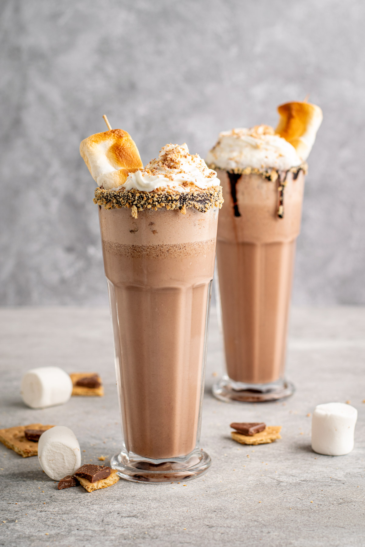 two s'mores milkshakes topped with whipped cream, graham crumbs, and toasted marshmallows.