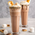 two s'mores milkshakes topped with whipped cream, graham crumbs, and toasted marshmallows.