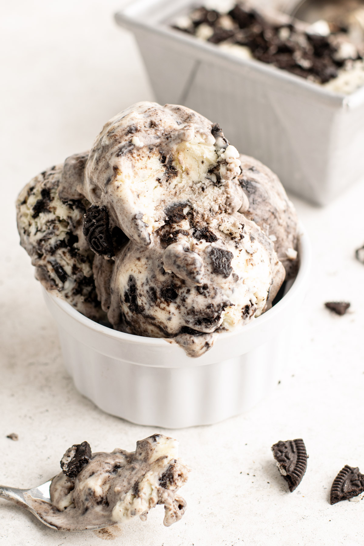 scoops of cookies and cream ice cream in a white ramekin with a spoon infront.