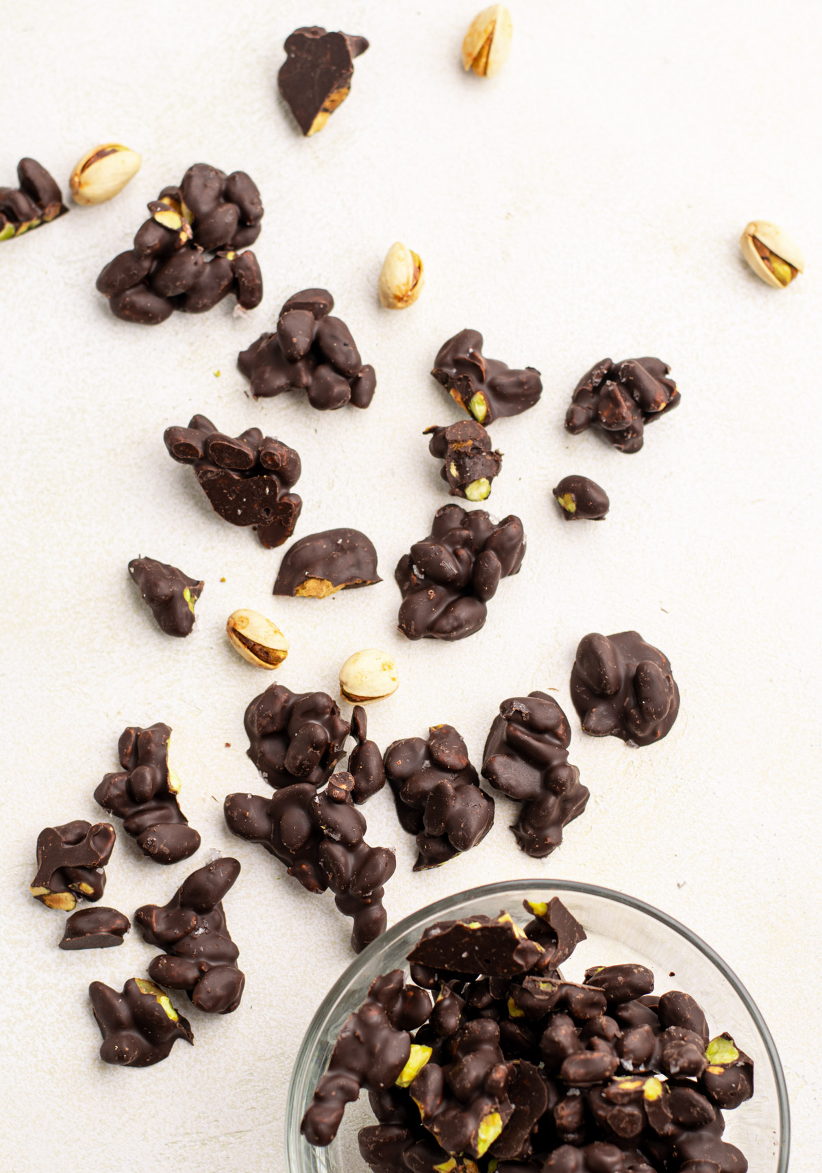 chocolate covered pistachio clusters scattered over a light backdrop.