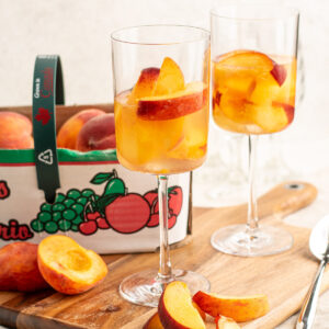 peaches and wine in 2 glasses with a basket of peaches behind.