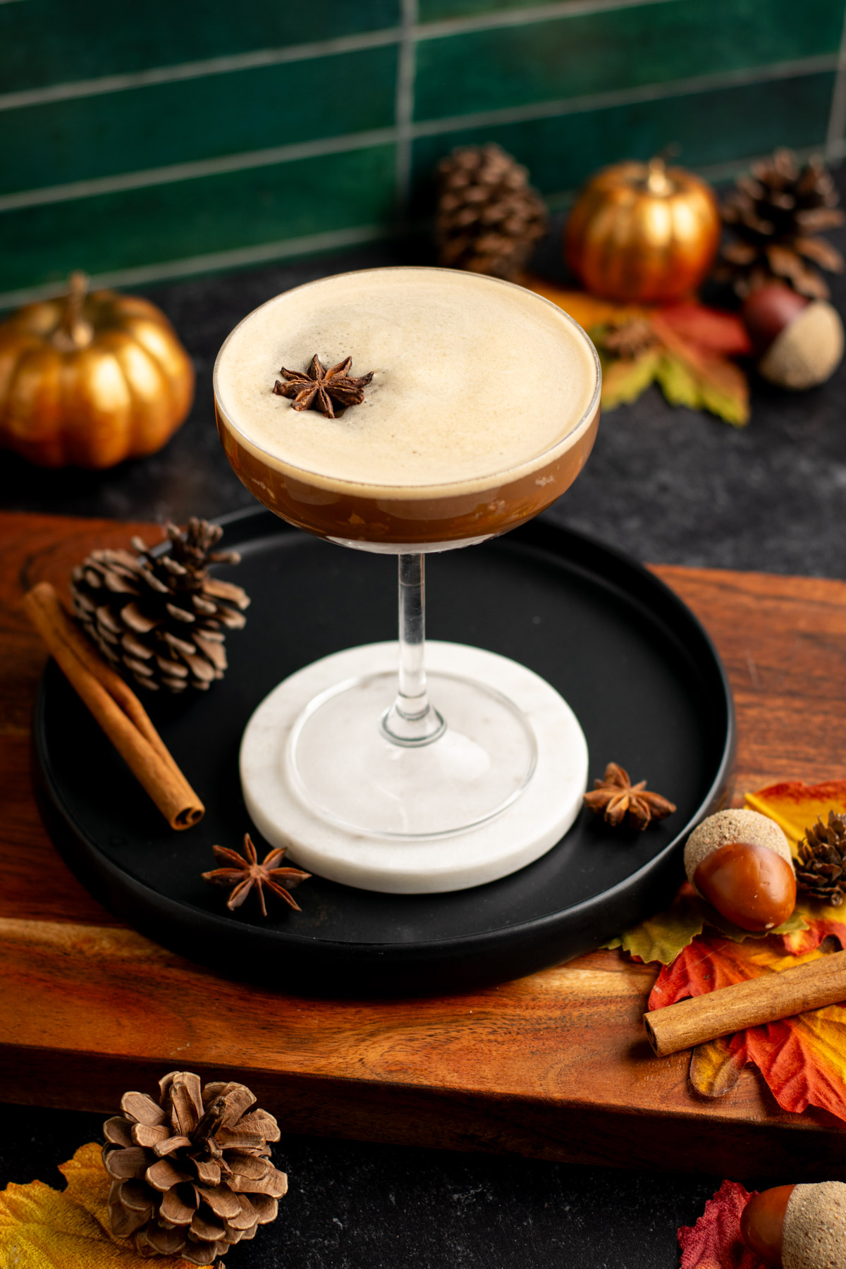 chai espresso martini on a black plate with fall leaves, acorns, and pinecones around.