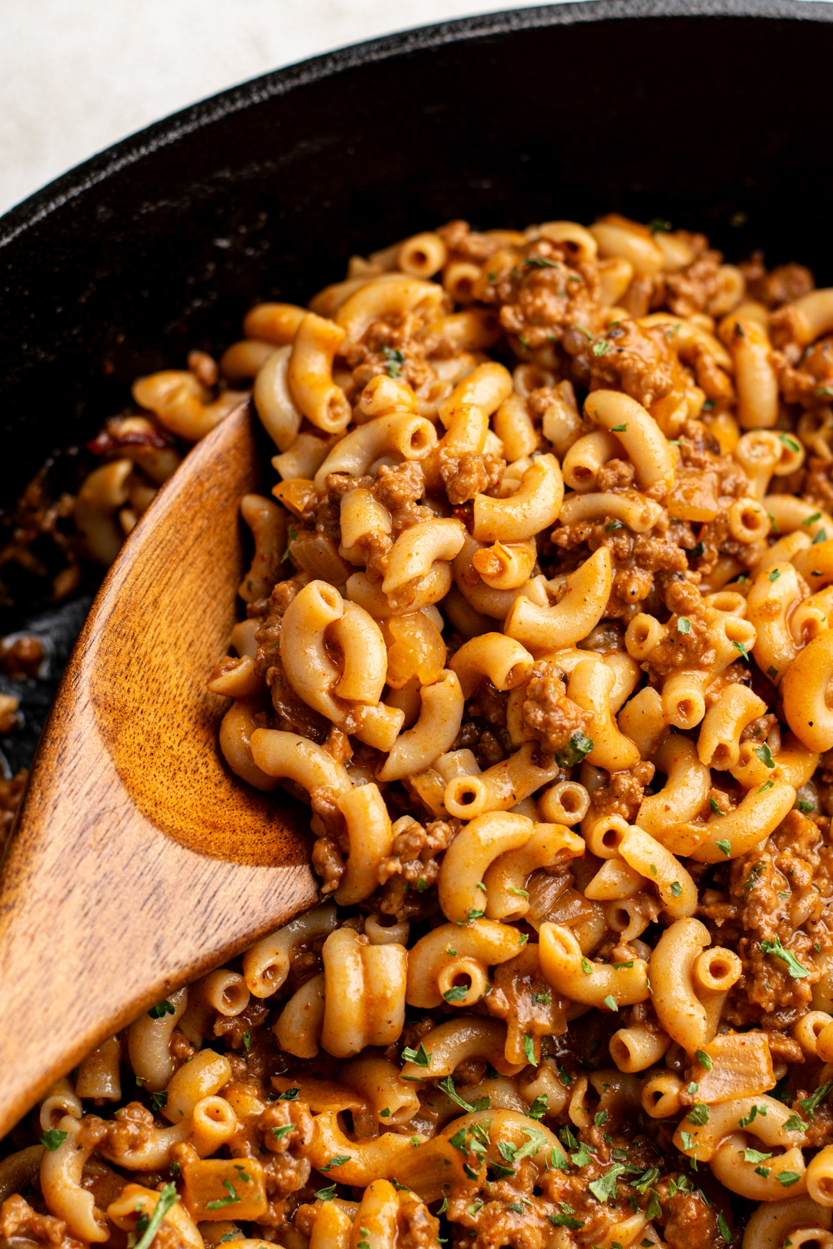 close up of wooden spoon scooping homemade hamburger helper from a cast iron skillet.