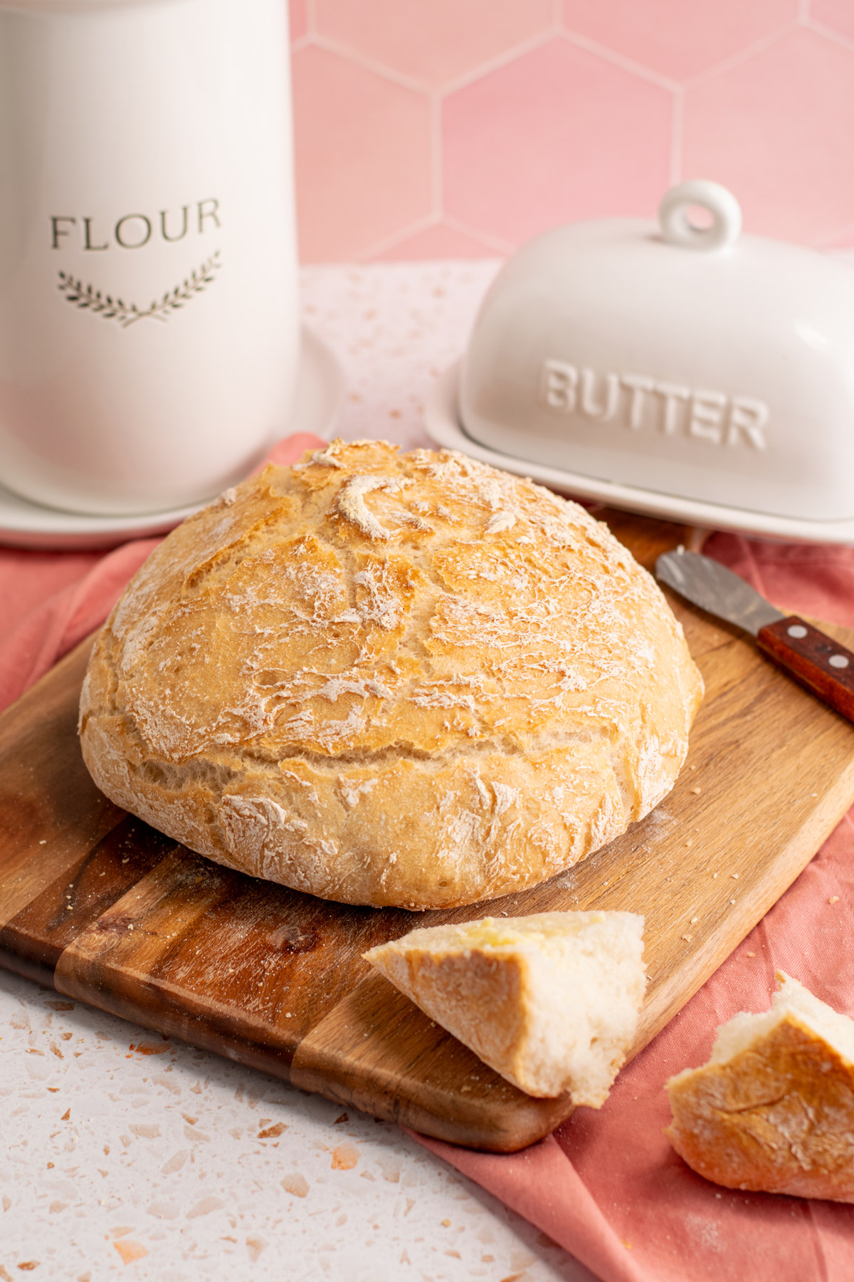 gluten free no knead bread on a wood board with butter and flour containers in the background.
