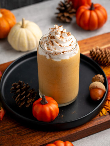pumpkin spice protein shape with whipped cream on top and pumpkins around.