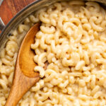 wooden spoon in a skillet of white cheddar mac and cheese.