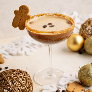 gingerbread espresso martini in a coupe glass with a gingerbread cookie hanging on the side.