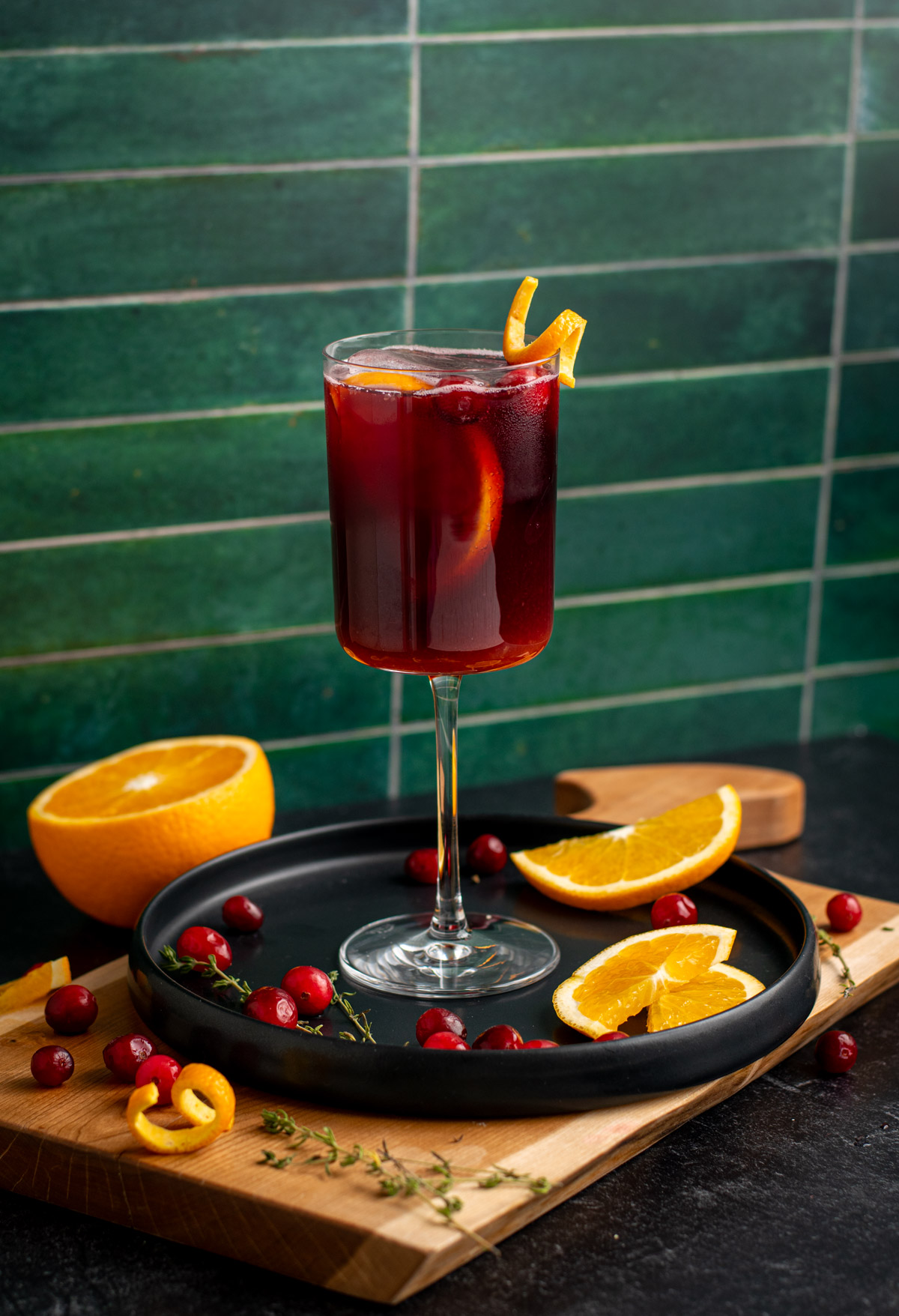 lambrusco spritz on a black plate with orange slices around and a green tile background.