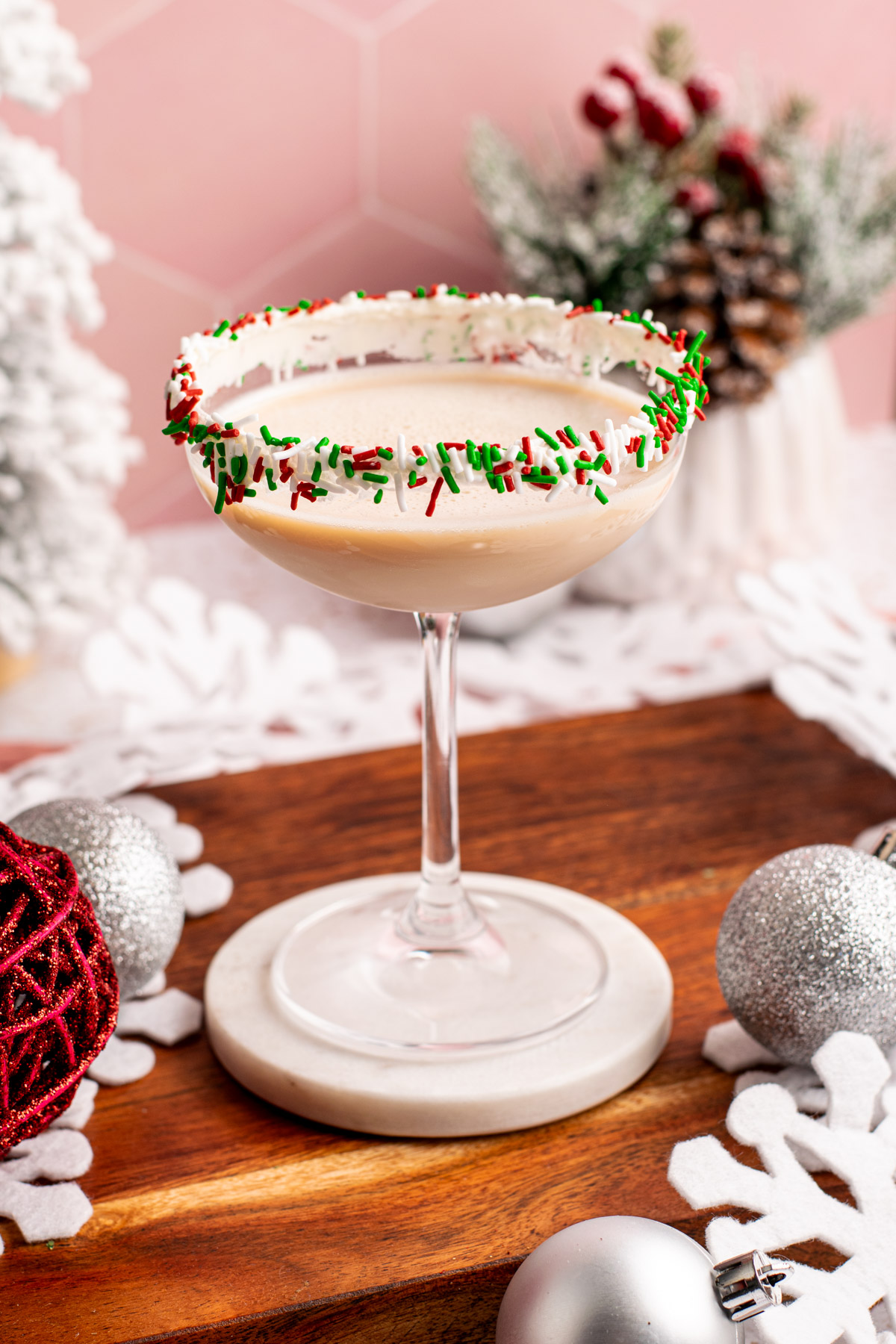 sugar cookie martini in a sprinkle-lined coupe glass with a pink background.