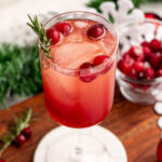 winter aperol spritz in a wine glass with cranberries and rosemary.
