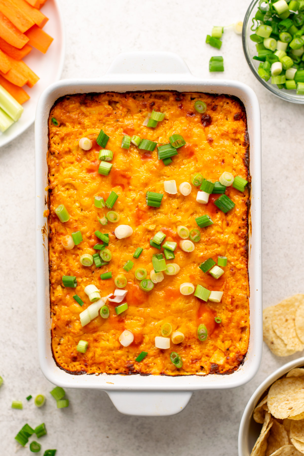 buffalo chicken dip in a white dish with green onions on top and tortilla chips in a bowl on the side.