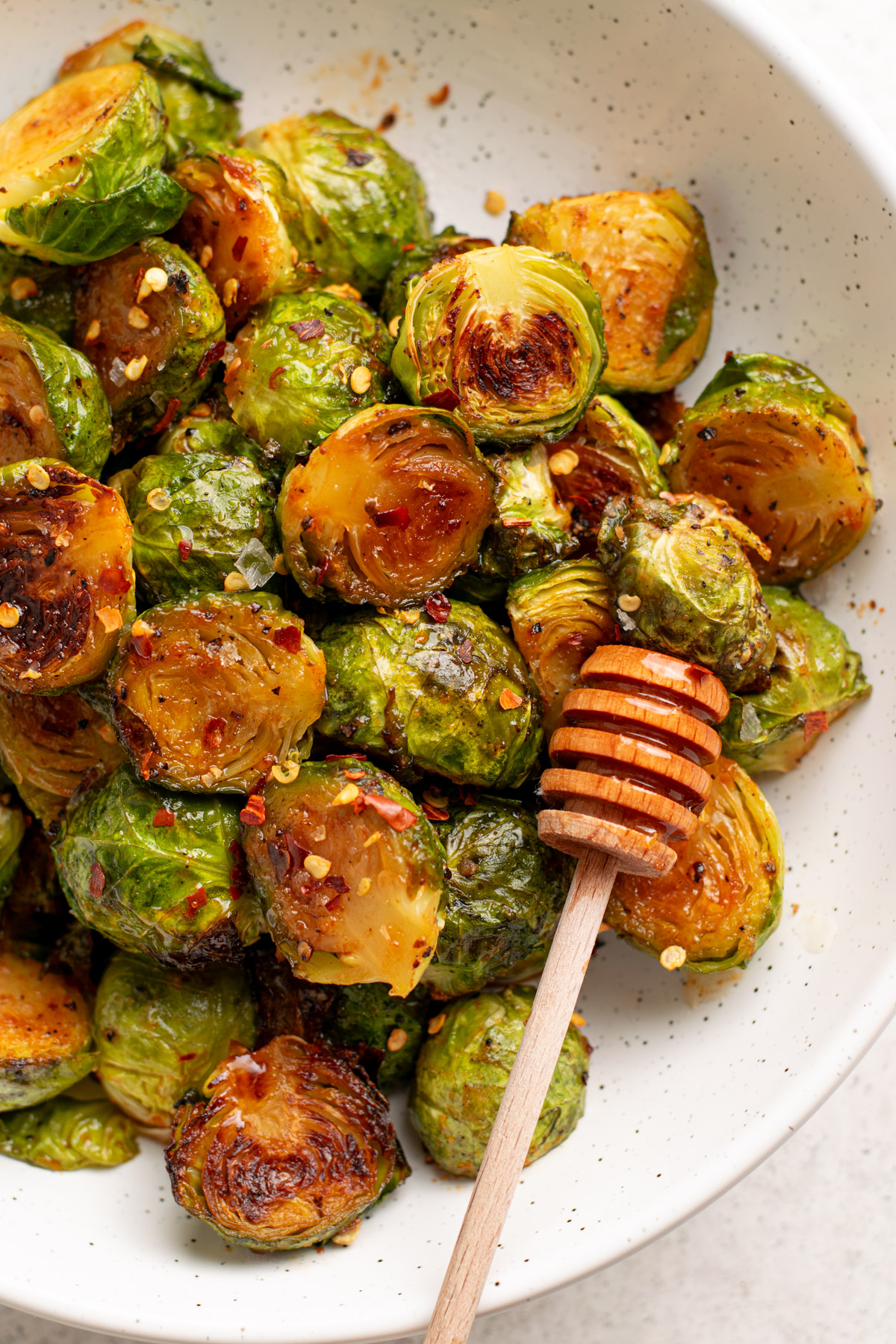 brussel sprouts in a white bowl topped with pepper flakes and a honey dipper.