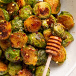 honey sriracha brussel sprouts in a white bowl with a honey dipper.