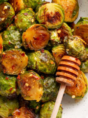 honey sriracha brussel sprouts in a white bowl with a honey dipper.