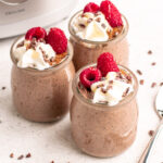 3 jars of blended chia pudding topped with whipped cream, raspberries, and cacao nibs.