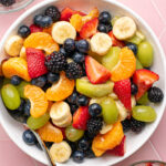 fruit salad in a white bowl on a pink background.