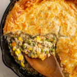 chicken pot pie skillet with a wooden spoon scooping filling.