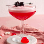pink lady mocktail in a coupe glass with cherries on top.