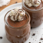 two jars of cottage cheese chocolate pudding topped with whipped cream and chocolate shavings.