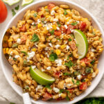 protein elote pasta salad in a white bowl with lime wedges.