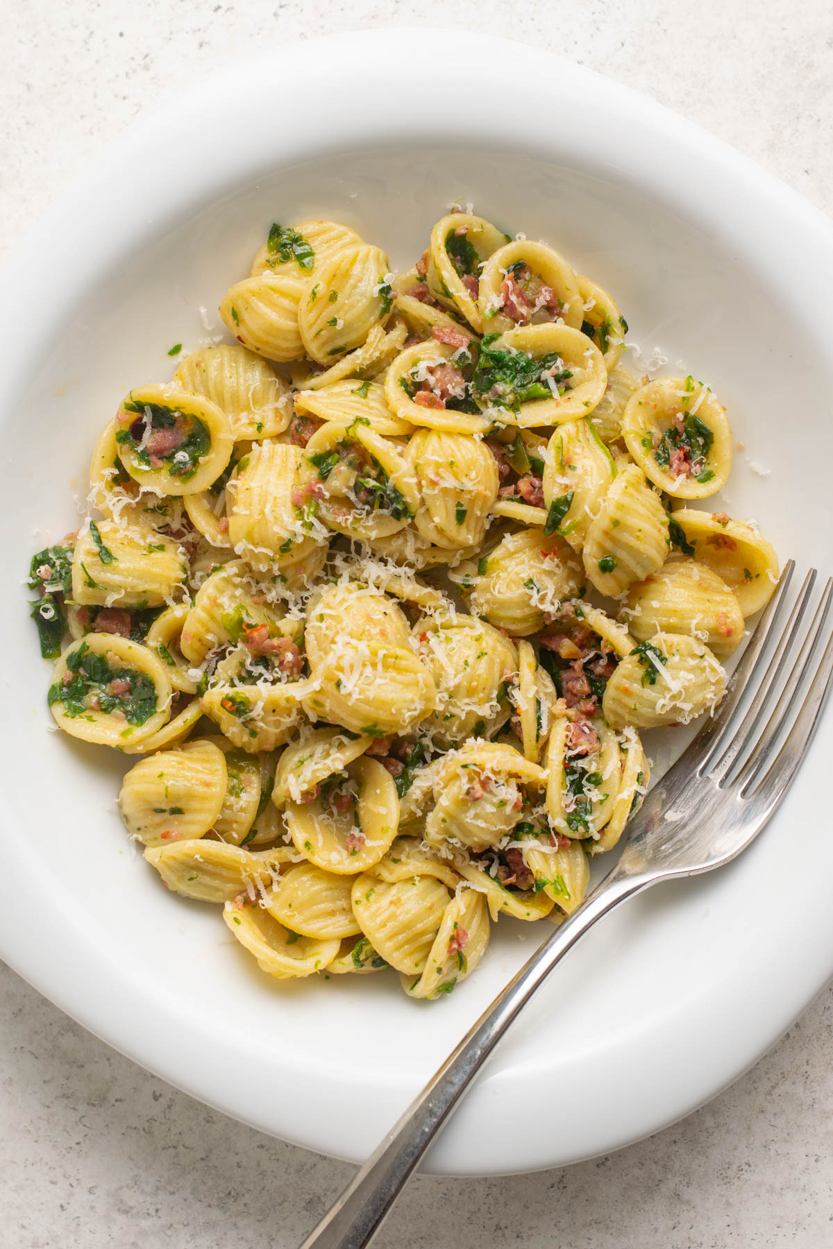 top view of a bowl of orecchiette pasta with spinach and salami.
