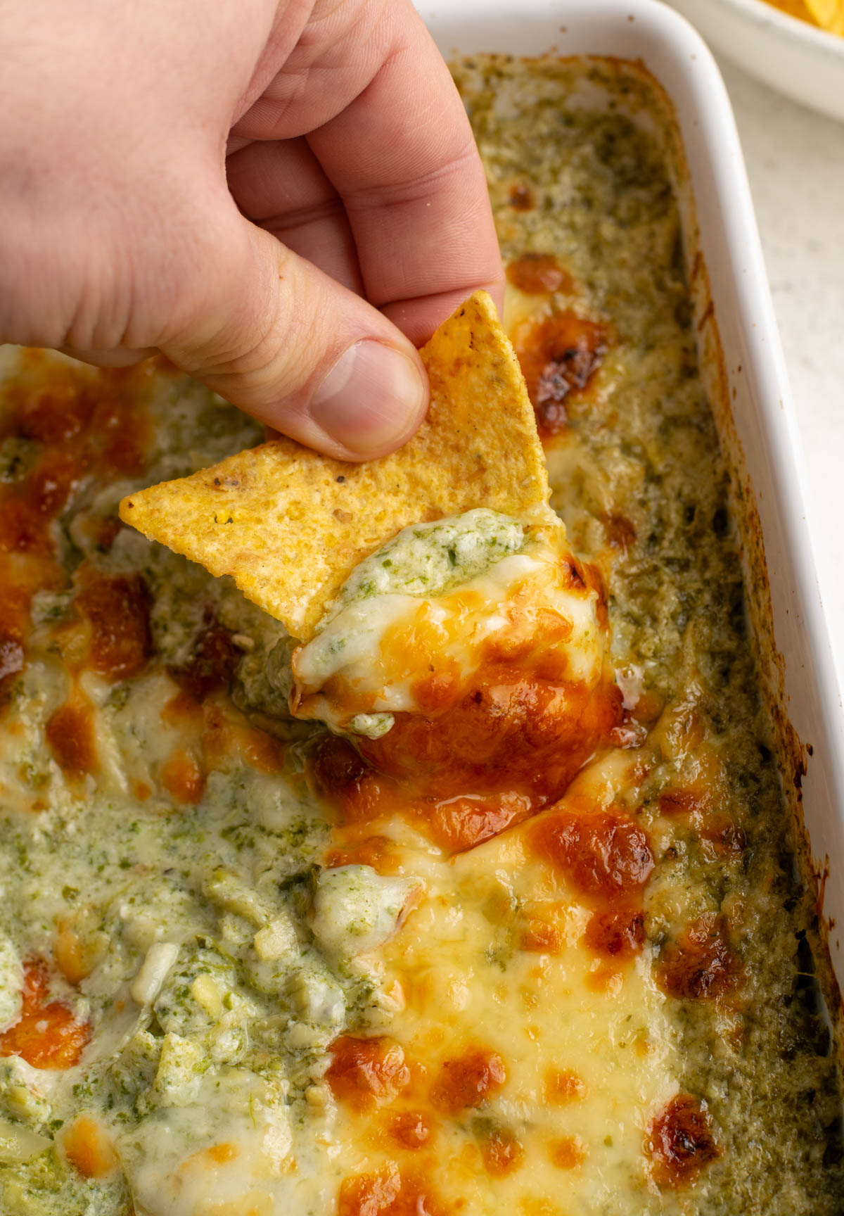 close up of tortilla chip scooping cheesy protein spinach dip.