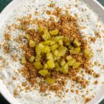 cottage cheese fried pickle dip in a bowl topped with breadcrumbs and chopped pickles.